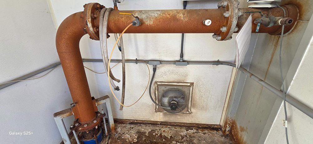 A heavily rusted industrial pipe system in a utility room before undergoing dustless blasting for corrosion removal.