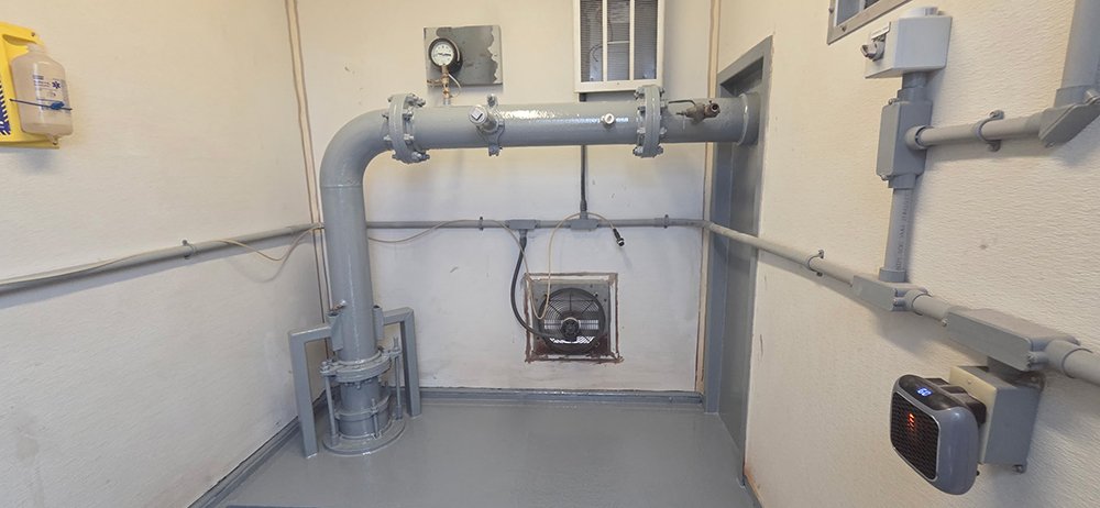 A clean, restored industrial utility room featuring a freshly coated grey protective epoxy floor and pipes after professional corrosion removal.