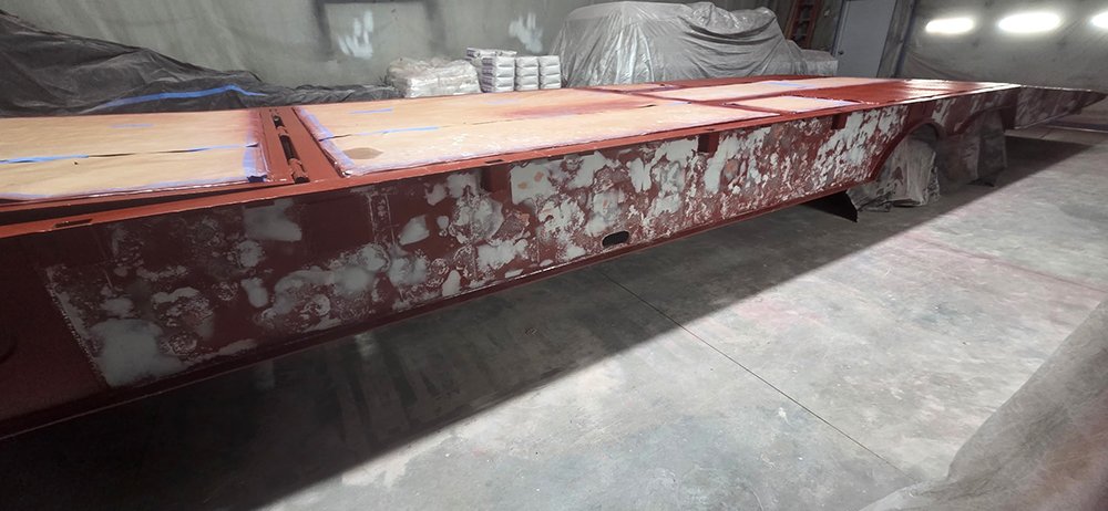 A long industrial flatbed trailer showing a detailed red oxide primer application after a full dustless blasting treatment.