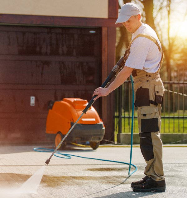 A professional technician using high-pressure washing equipment to clean a brick paver driveway.
