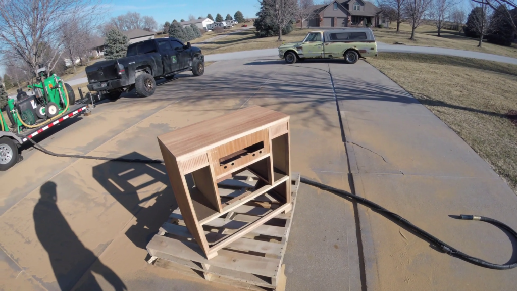 A wooden console cabinet being stripped of old finish using eco-friendly dustless blasting on a residential driveway.