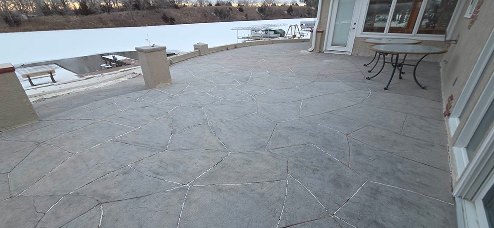 A wide view of a clean, restored stamped concrete patio on a waterfront property after the removal of old red paint.